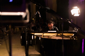 man playing grand piano at a night concert, general shot, between the spotlights - obrazy, fototapety, plakaty