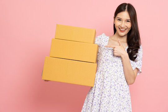 Young Asian woman holding package parcel box isolated on pink background, Delivery courier and shipping service concept