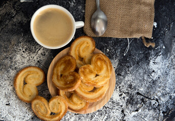 Deliciosos pasteles palmeritas, orejitas con taza de café sobre fondo oscuro.
