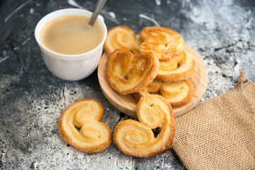 Deliciosos pasteles palmeritas, orejitas con taza de café sobre fondo oscuro.