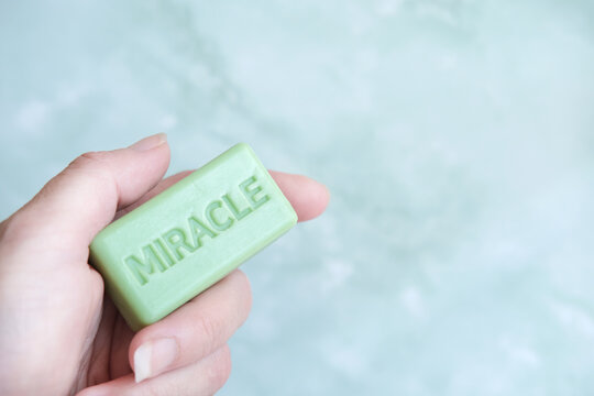 closeup of hand holding a small soap against mabrble bathroom cramic tile 