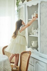 A preschool girl takes out a jar of cookies from the sideboard. Retro interior.