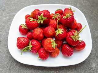 Ripe juicy fruits of garden strawberries on a rectangular white plate on a gray concrete surface, summer harvest, healthy breakfast.