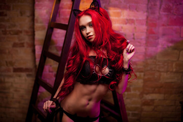 Beauty fashion model Girl with red hair on an antique bed. In the background is a ladder. A young...