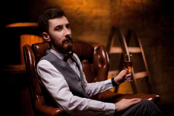 A bearded young man sommelier tries white wine in a glass. Close -up portrait of professional...