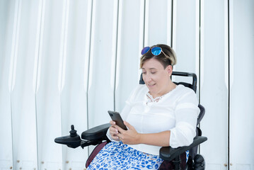 Fototapeta na wymiar portrait of a smiling woman with disability in a wheelchair looking at her smartphone on a white background