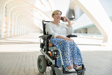 an elegant and smiling woman with disability sitting in a wheelchair talking on a mobile phone