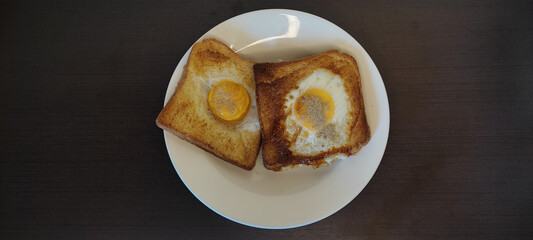Sliced ​​bread stuffed with fried egg in the middle Baked crisps are placed in a white plate, black wooden floor, garnished with pepper. from top view