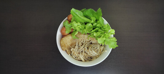 The white bowl contains fish, green vegetables and sausages. Placed on a black wooden table, top view.