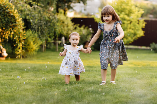Two happy girls, adorable sisters are smiling happily together. Child girl holding hand her younger baby sister and playing outdoors on summer day holiday vacation, best friends.Family day