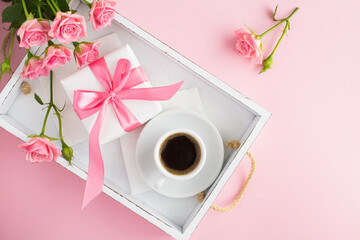 Obraz na płótnie Canvas Coffee in the cup, gift box and pink roses on the white wooden tray on the pink background. Top view. Copy space.