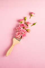 Paintbrush with pink roses on the pink background. Top view. Location vertical.