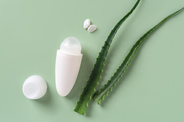 Roll on antiperspirant deodorant, two fresh aloe leaves and sea shell butterfly over pastel green...