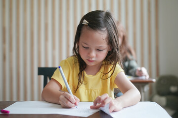 Preschool kids drawing with color pencil on white paper on table in classroom with friends, kindergarten education concept