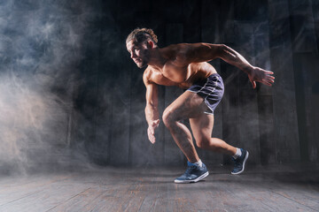 Strong athletic man sprinter ready to run. Professional athlete, runner training on dark background. Muscular, sportive male in dynamic movement. Concept of sport healthy lifestyle, fitness motivation