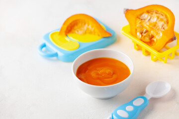 Pumpkin puree in a bowl and toy plastic tableware. Baby food concept.