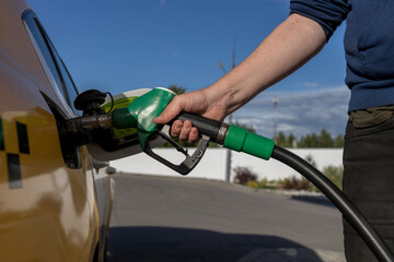 A man refueling a car at a gas station. The taxi driver pours fuel into the tank of the car. A man holds a refueling pistol in his hand.