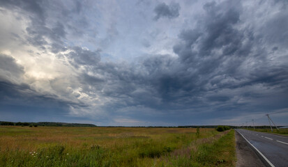 Dramatic sky over road and field. Evening rural landscape with thunderclouds.