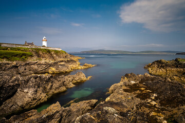Fototapeta na wymiar rocky shoreline with turquoise pools and the historic Broadhaven Lighthouse on a clifftop promontory