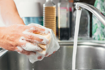Young woman's hands washing a white cup with water and dish soap. Close-up of female hands rinsing...