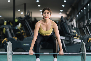 Beautiful Asian woman working out in the gym to stay fit and strong and gain beautiful muscles by lifting weights.