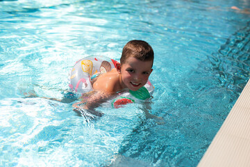 A little boy swims in a beautiful blue pool in an inflatable circle.