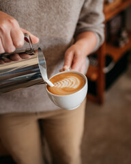 Person pouring a cappuccino into a coffee cup