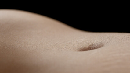 Macro shot of belly of young African American slim female model on black background | Skin texture shot for body care concept