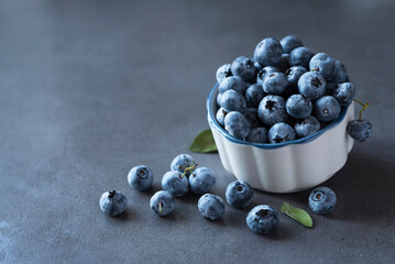 Fresh blueberry in a clay bowl and scattered berrues around on the dark grey background. Copy space. Flat lay. Healthy nutrition