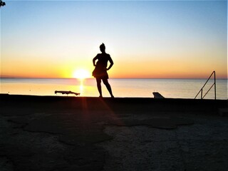 Tourism. Journeys. Sea. Beautiful sunset. Black silhouette of a girl in a dress.