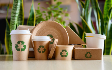Paper eco-friendly disposable tableware with recycling signs on the background of green plants. The concept of using biodegradable materials. - obrazy, fototapety, plakaty
