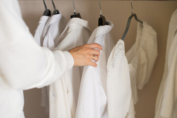A girl in white clothes hangs light things in a closet on a hanger