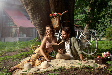 Picnic of couple man and woman sitting on rug under tree in park over vintage bicycle background....