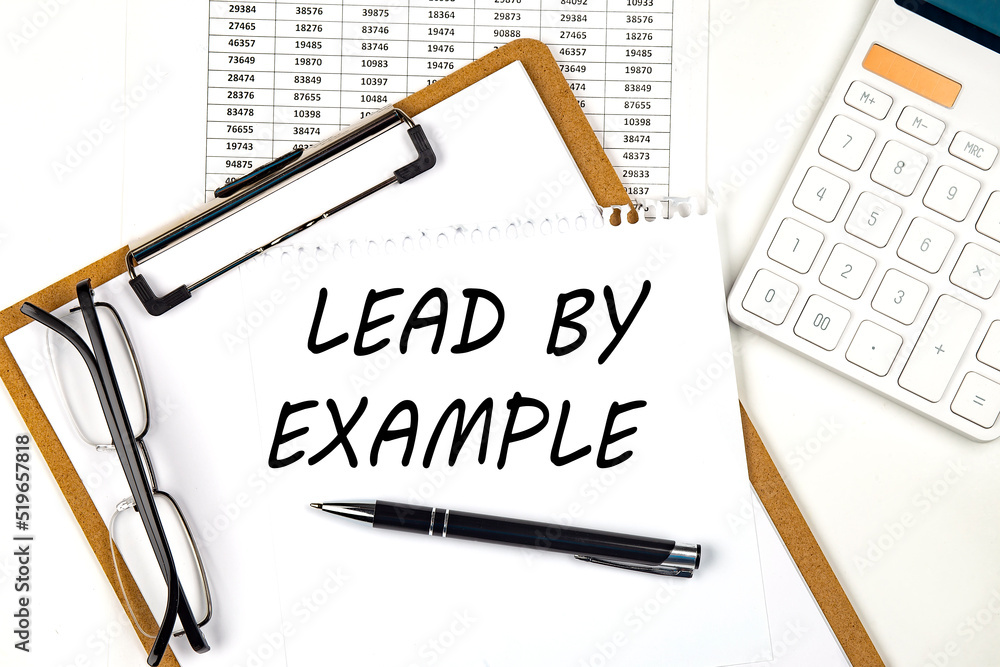 Poster text lead by example on the white paper on clipboard with chart and calculator