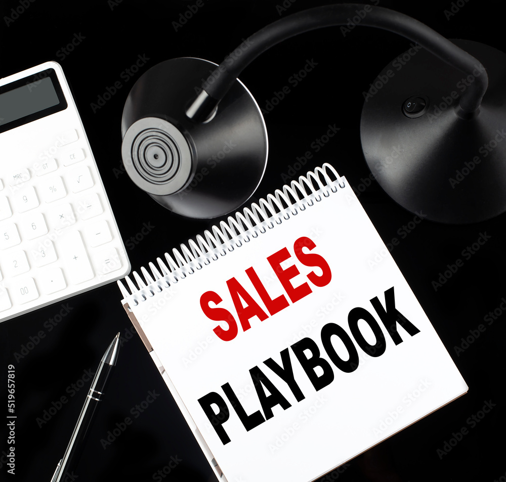 Poster opened paper notebook with text sales playbook with a pen, calculator and table lamp on black backgr