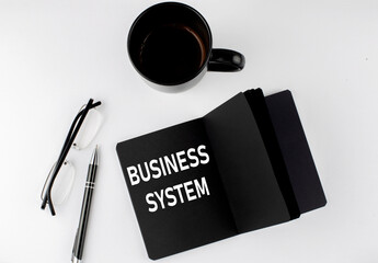 BUSINESS SYSTEM written text in small black notebook with coffee , pen and glasess on white...