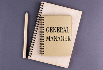 Word GENERAL MANAGER on notebook with pencil on the grey background