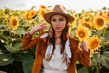 boho, bohemian style girl in a field of sunflowers, summer mood, hot season. Hat, long dress, feathers, hippies