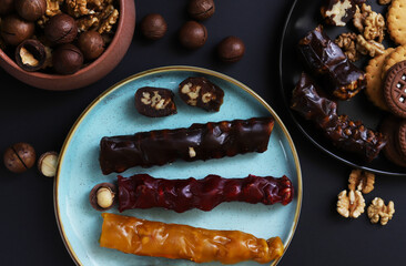 Churchkhela is a sweet delicacy of nuts in juices thickened with flour. Georgian churchkhela in a plate on a dark table with nuts. Close-up