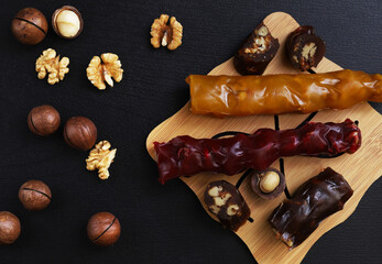 Churchkhela is a sweet delicacy of nuts in juices thickened with flour. Georgian churchkhela in a plate on a dark table with nuts. Close-up
