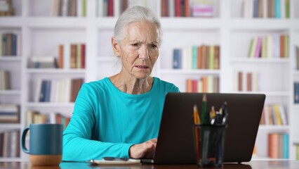 Closeup of senior older woman online concept, video chat, watching business training class, live webinar on laptop computer remote working, social distance learning, writing notes from home office.