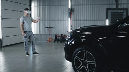 In car service mechanic in uniform checking and diagnosing a car with a breakdown after a crash using modern virtual reality glasses with controllers