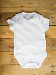 Flat lay of a white baby bodysuit for newborn boys and girls made of cotton on a wooden background. Close-up. Layout for the design and placement of prints, logos, advertising.