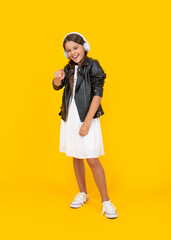 happy teen girl listen music in headphones on yellow background. pointing finger