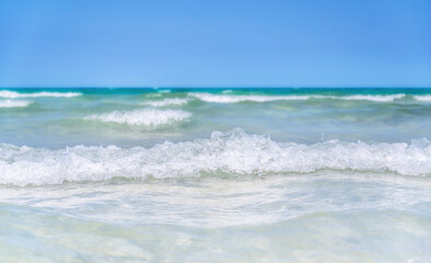 Fototapeta na wymiar Kleine Wellen in einer türkis blauen Brandung eines tropischen Meeres vor wolkenlosem Himmel
