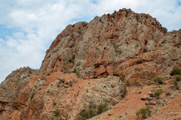Red mountains and rocks covered green vegetation under cloudy sky in Armenia near Noravank monastery 