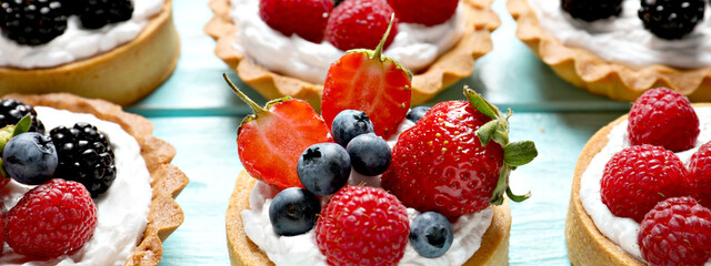 Delicious tartlets with fresh berries on light blue wooden table, closeup. Banner design