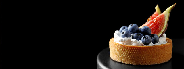 Delicious tartlet with fresh blueberries and figs on cake stand against black background, space for...