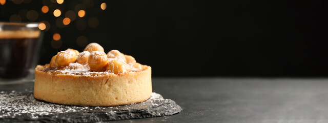 Delicious tartlet with hazelnuts, sweet caramel and powdered sugar on black table, space for text....