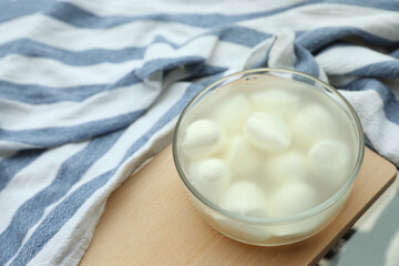 Delicious mozzarella in glass bowl on wooden board, above view. Space for text